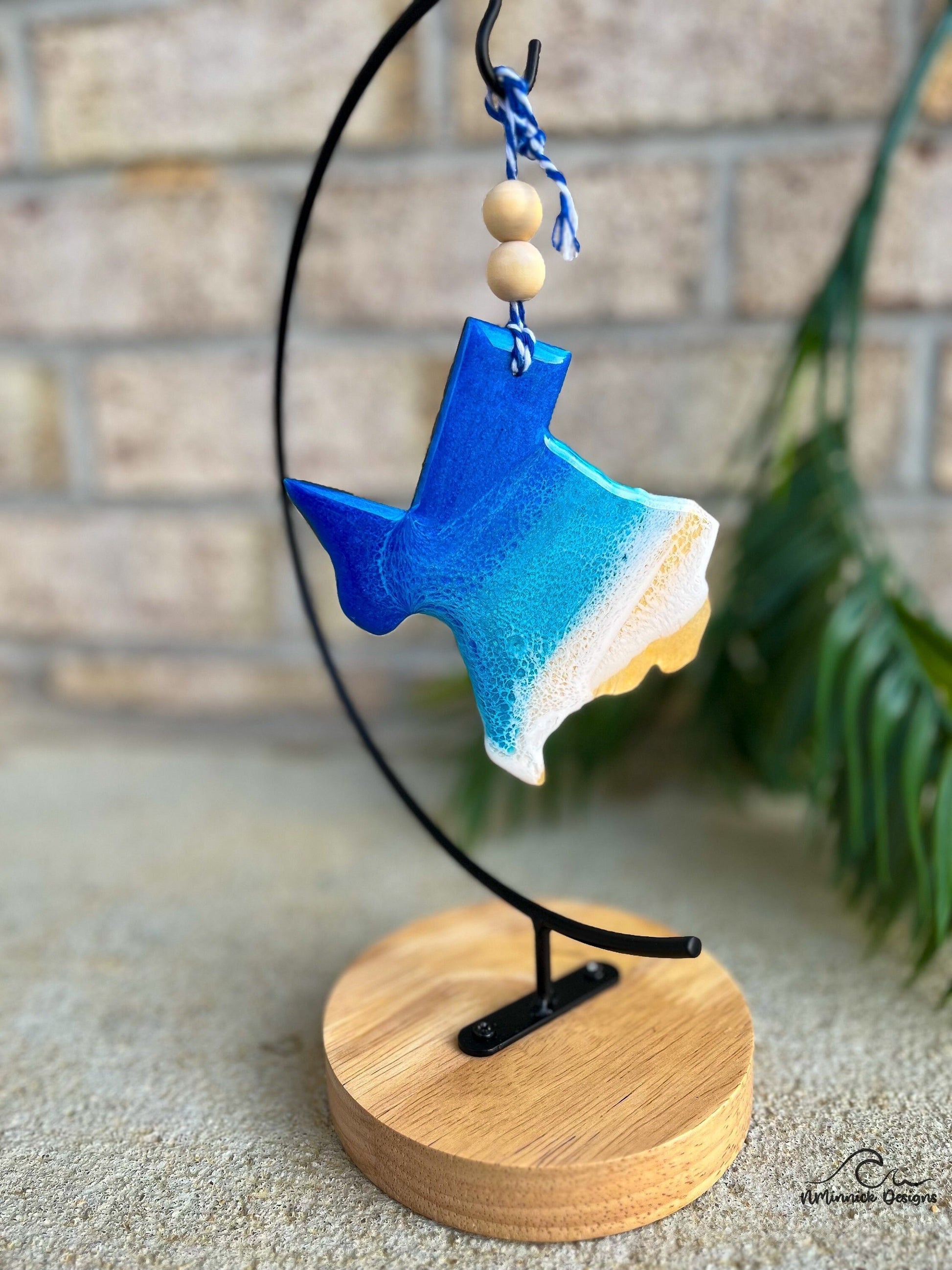 Texas shaped wooden ornament with ocean resin waves on the front hanging from blue and white twine with two wooden beads shown on an ornament hanger