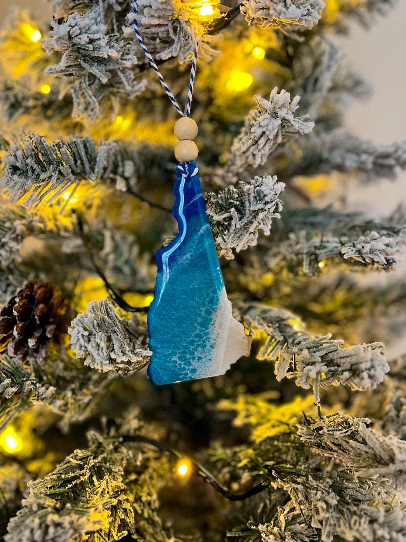 Handmade New Hampshire shaped wooden ornament featuring ocean resin waves, finished with blue and white twine and two natural wooden beads