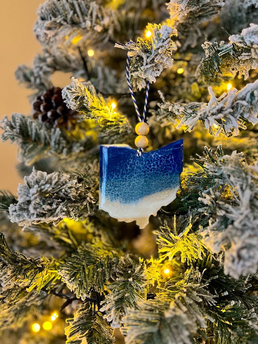 Handmade Ohio shaped wooden ornament featuring resin waves, finished with blue and white twine and two natural wooden beads