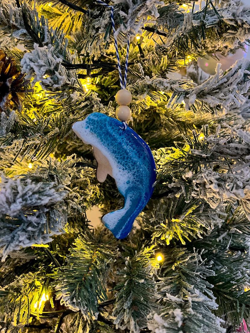 Handmade Manatee shaped wooden ornament featuring ocean resin waves, finished with blue and white twine and two natural wooden beads