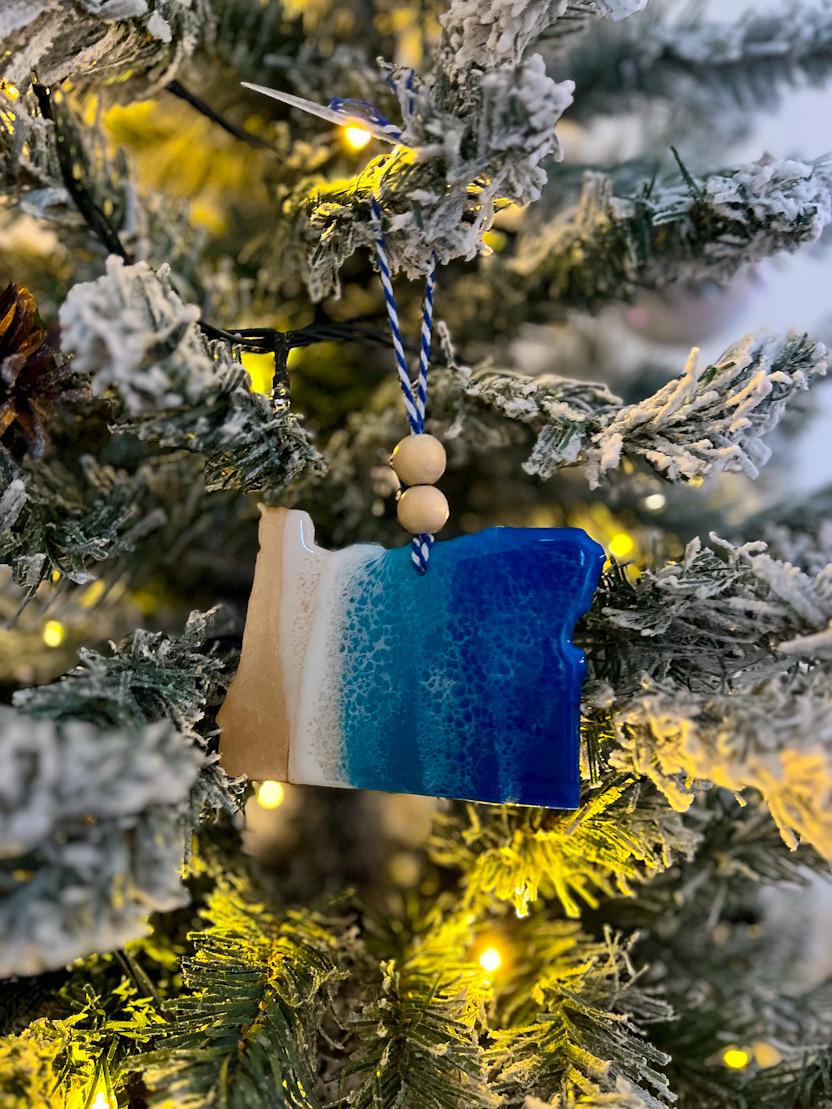 Handmade Oregon shaped wooden ornament featuring ocean resin waves, finished with blue and white twine and two natural wooden beads