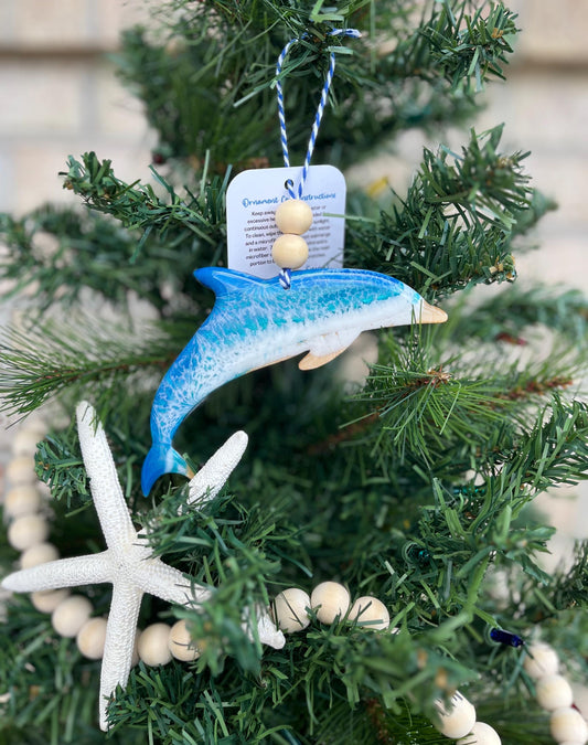 a Dolphin ornament with ocean resin art and finished with two wooden beads and blue and white twine. Hanging on a Christmas tree with a wooden garland and starfish.
