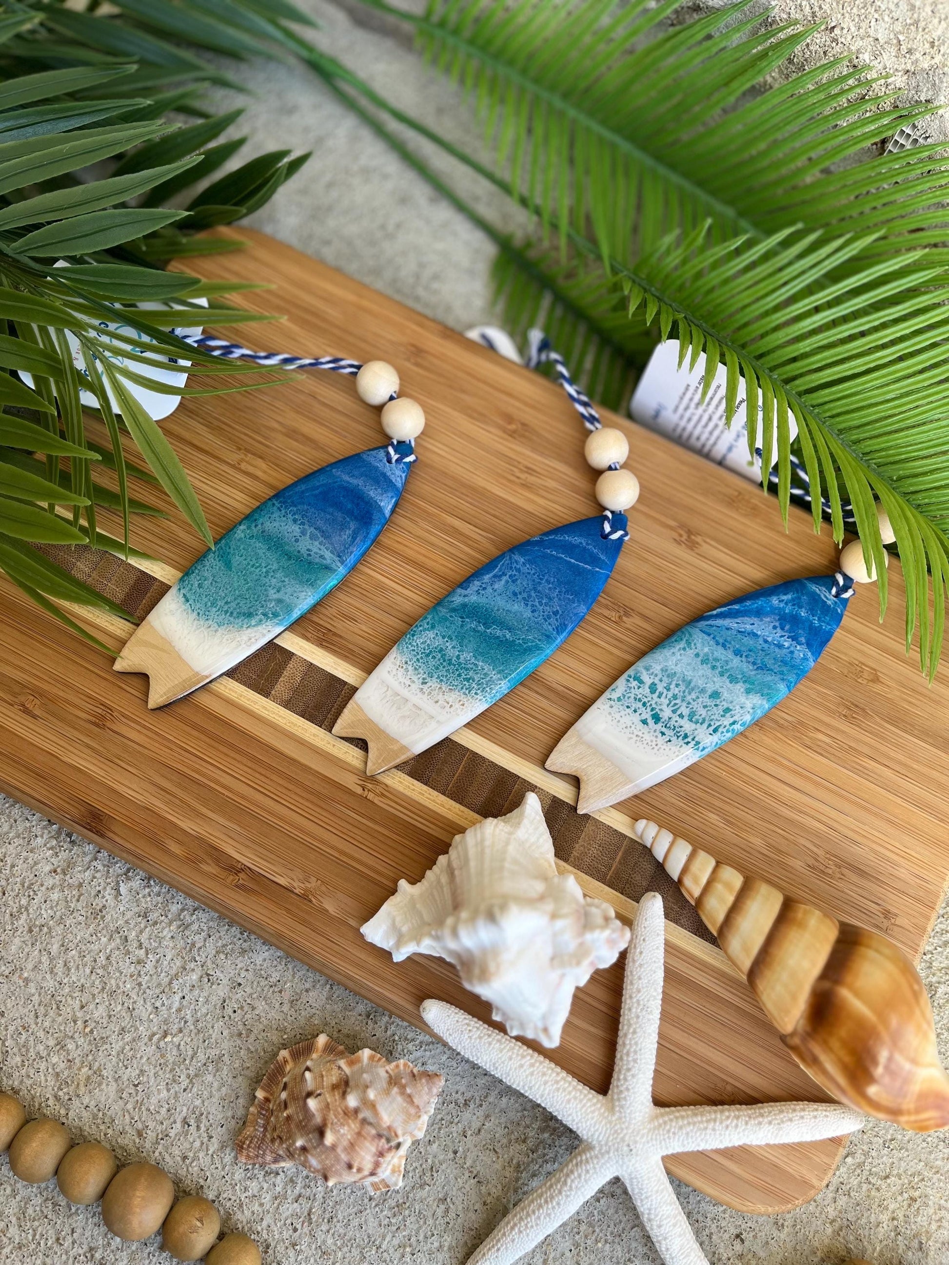 Three surf board ornaments laying against a bamboo board among seashells and palm leaves