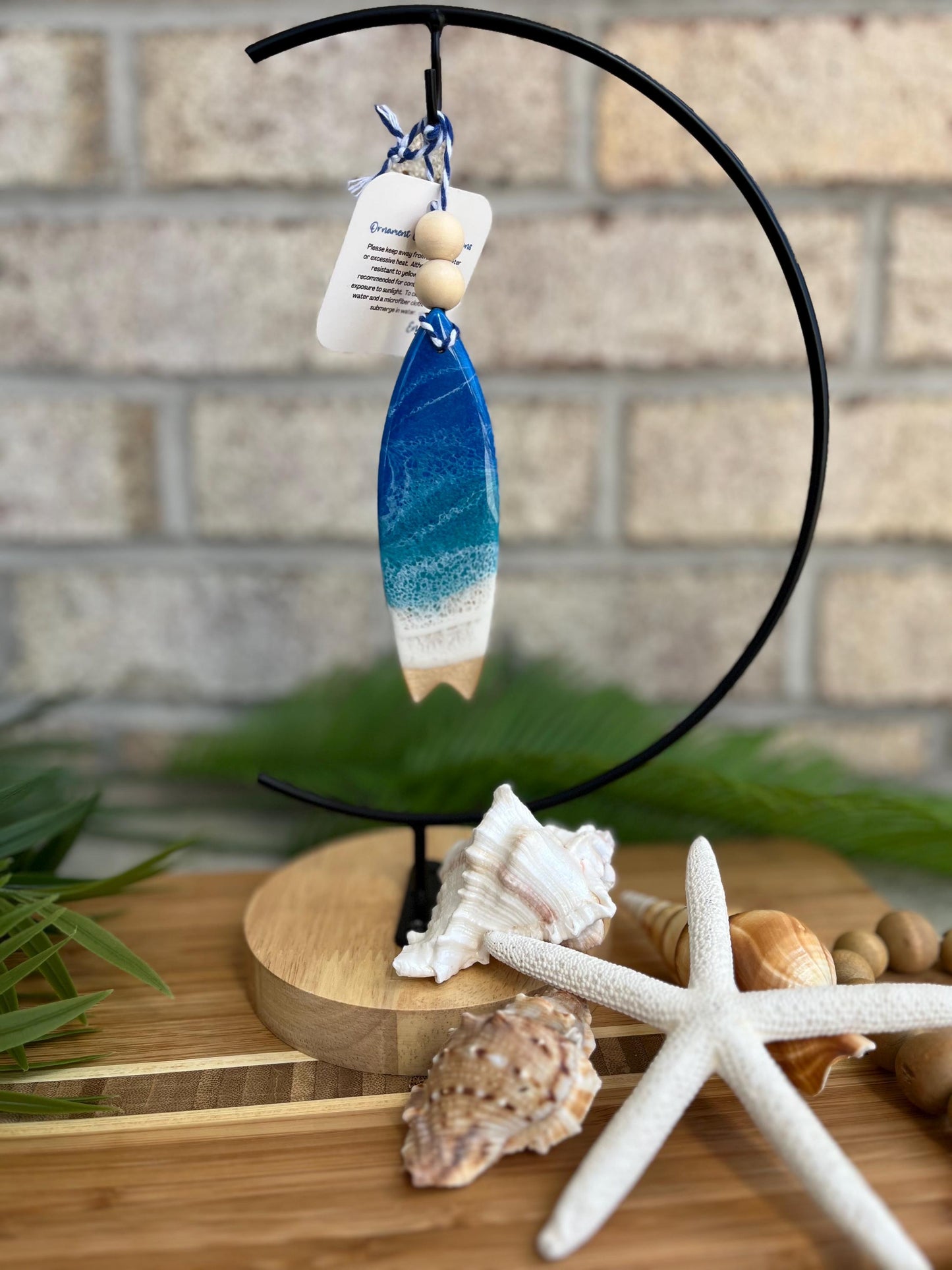 Surfboard Ornament with Ocean Resin Art hanging from an ornament hanger with seashells and a starfish.