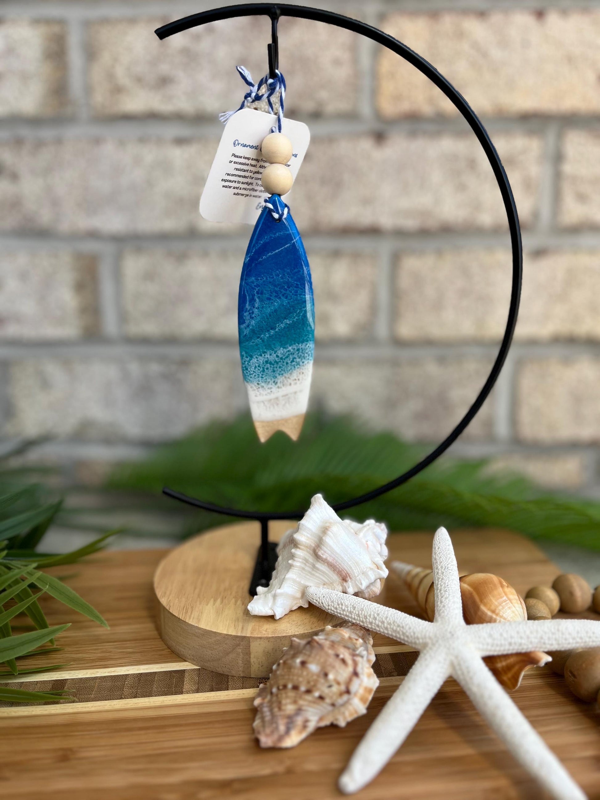 Surfboard Ornament with Ocean Resin Art hanging from an ornament hanger with seashells and a starfish.
