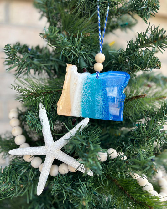 Oregon ornament featuring ocean resin art and finished with two wooden beads and blue and white twine. Hanging on a christmas tree with a wooden garland and a starfish.