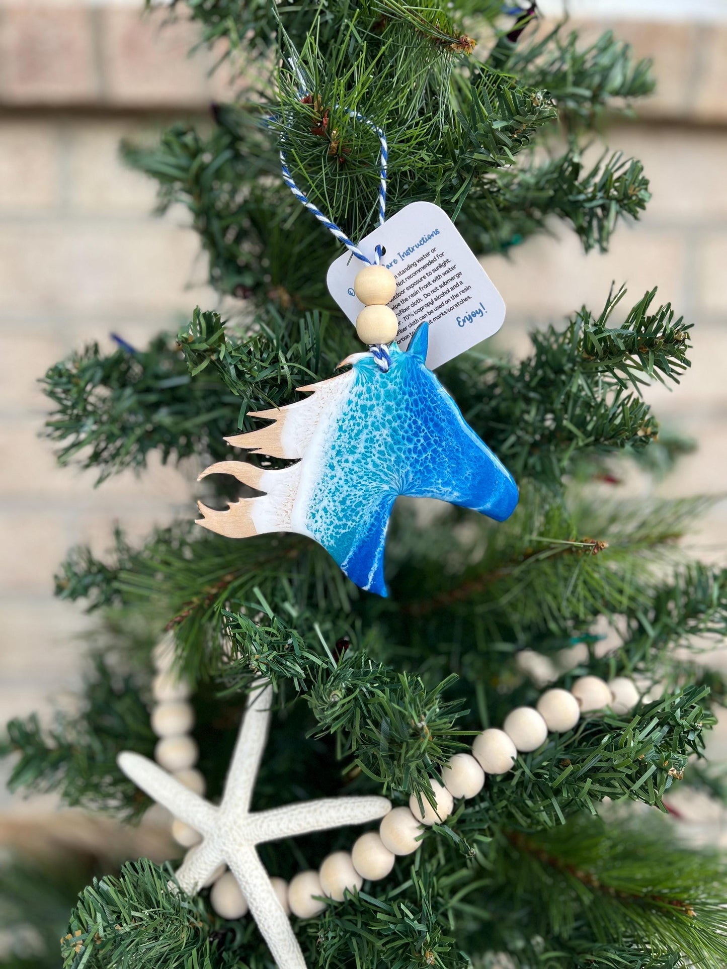 Horse ornament with ocean resin art and finished with two wooden beads and blue and white twine. Inspired by the wild horses on the Outer Banks and Shackleford Banks. Hanging on a christmas tree with a wooden garland and starfish.