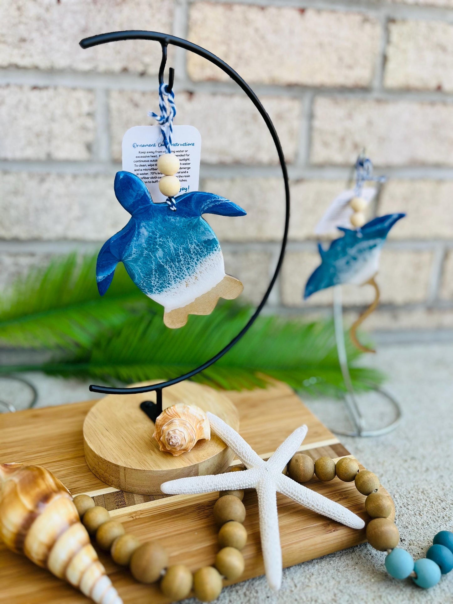 Sea Turtle Ocean Resin Ornament hanging on an ornament hanger amongst seashells, a starfish, wooden garland, and bamboo board.