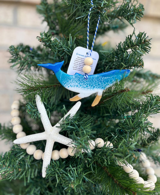 Humpback Whale Ornament featuring ocean resin art and finished with two wooden beads and blue and white twine. Hanging on a Christmas tree with a wooden garland and starfish.