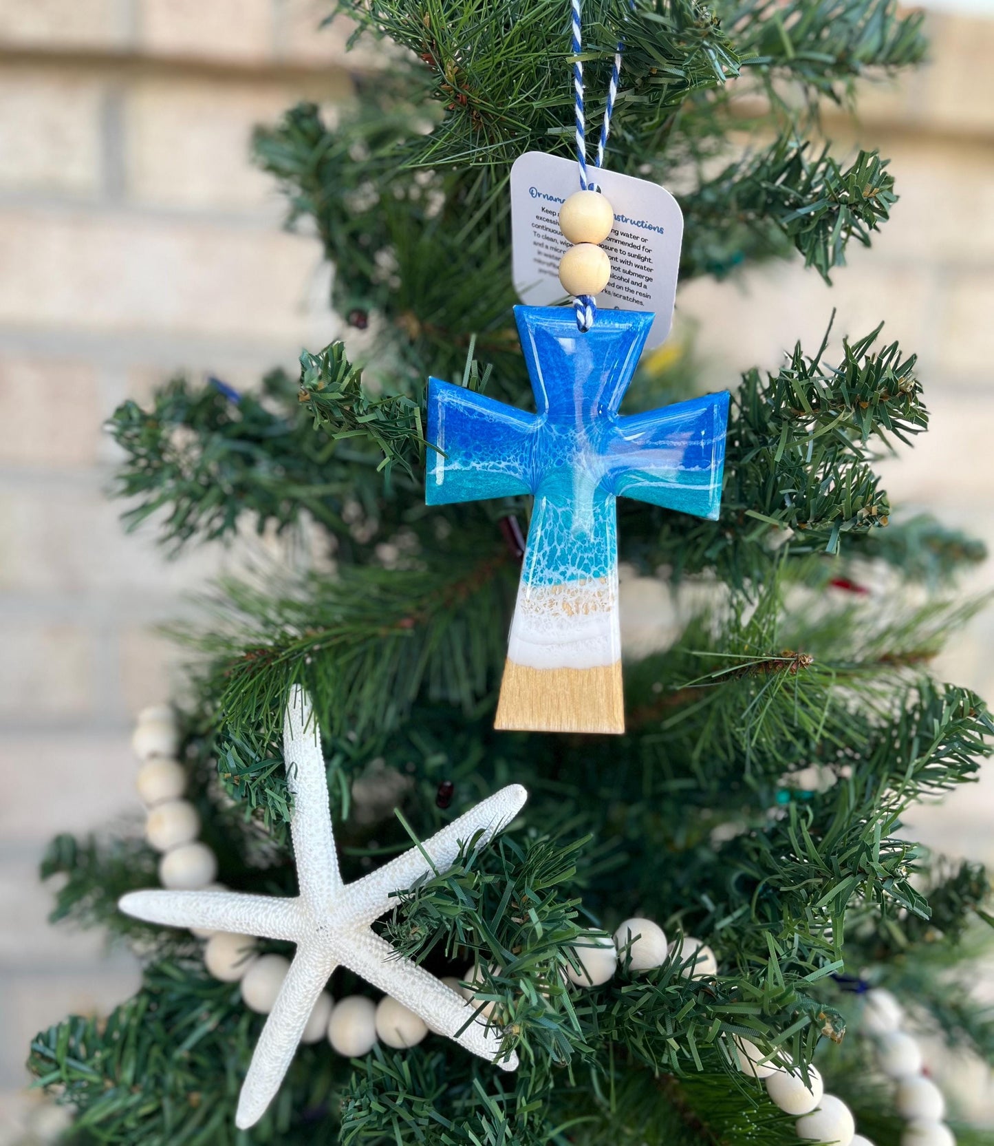 Handmade wooden and resin cross ornament featuring blue and white ocean resin waves and finished with two wooden beads and blue and white twine