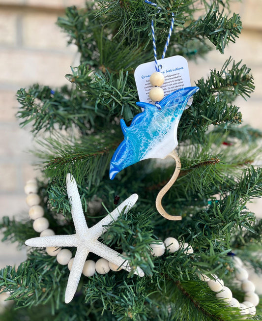 Manta Ray Ornament with ocean resin art and finished with two wooden beads and blue and white twine hanging on a christmas tree with wooden bead garland and a starfish