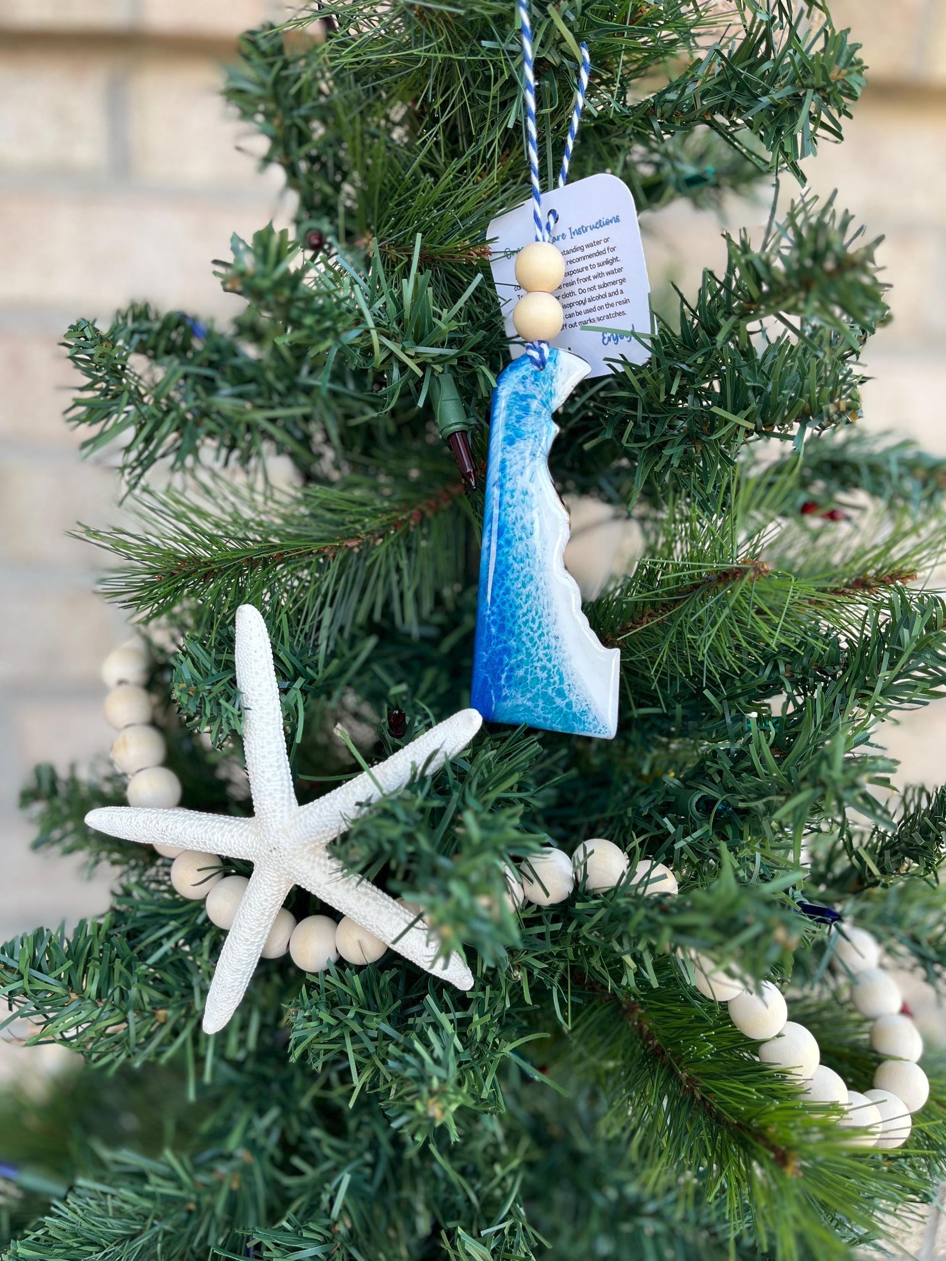 Delaware ornament with ocean resin art and finished with two wooden beads and blue and white twine. Hanging on a Christmas tree with a wooden garland and a starfish.