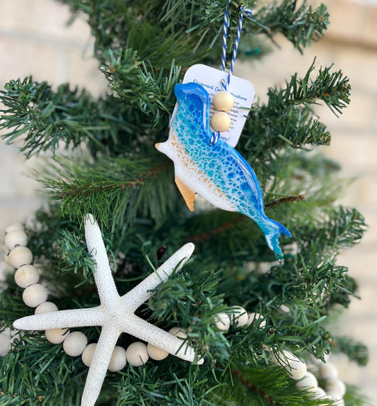 A Harbor Seal ornament with ocean resin art and finished with two wooden beads and blue and white twine. Hanging on a Christmas tree with a wooden garland and a starfish.