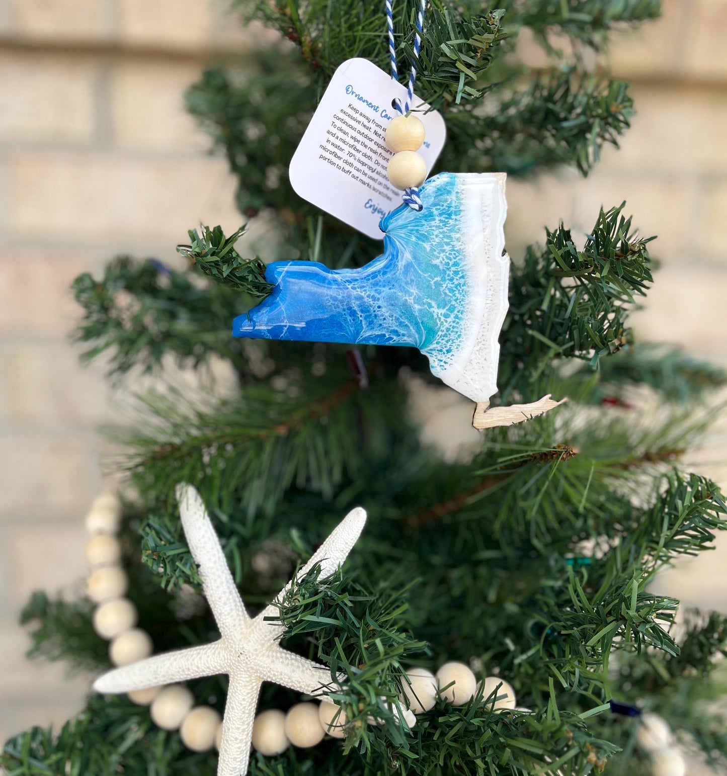 New York ornament with ocean resin art and finished with two wooden beads and blue and white twine. Hanging on a Christmas tree with a wooden garland and starfish.