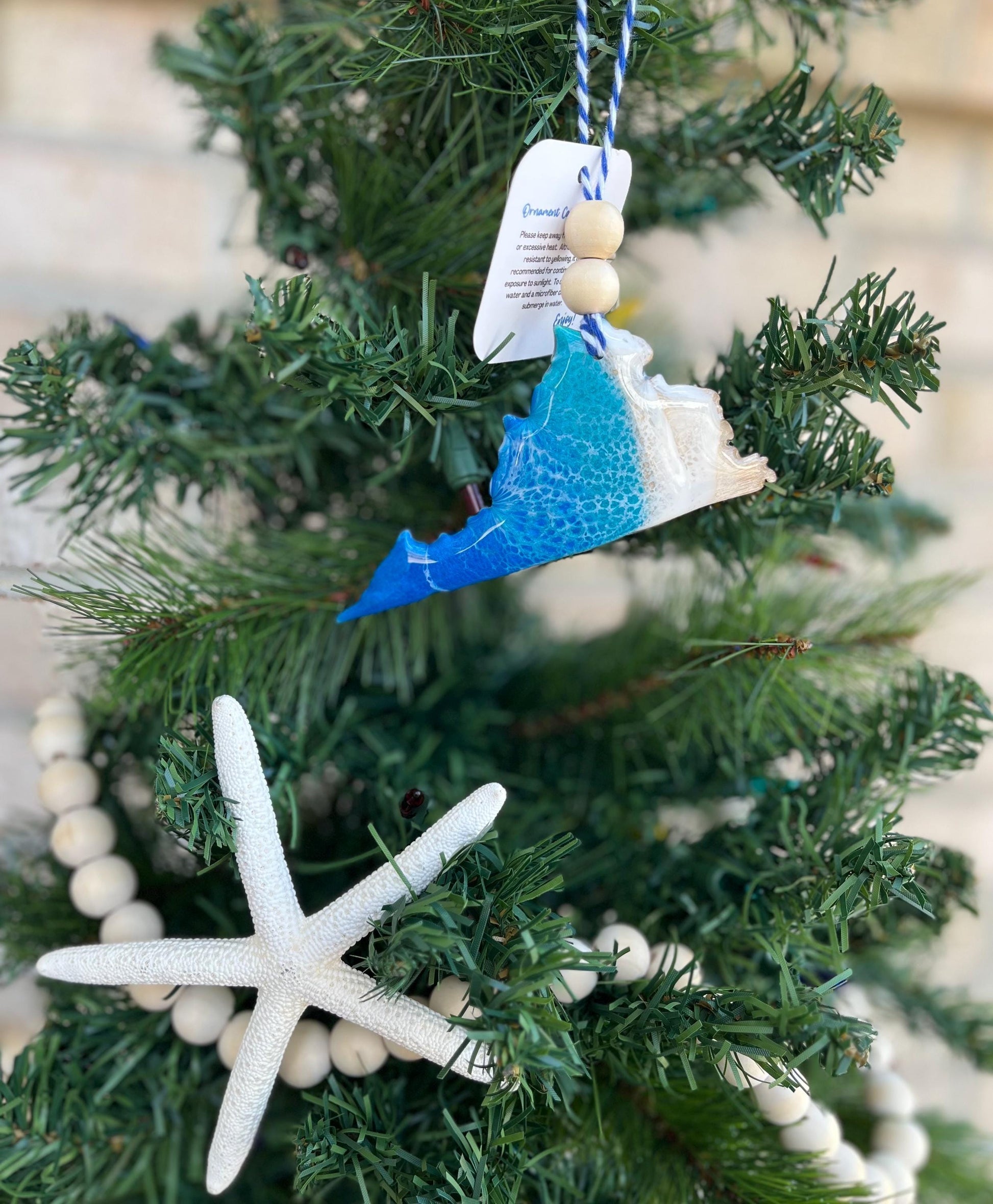 Virginia ornament featuring ocean resin waves and finished with two wooden beads and blue and white twine. Hanging on a christmas tree with a wooden bead garland and a starfish.
