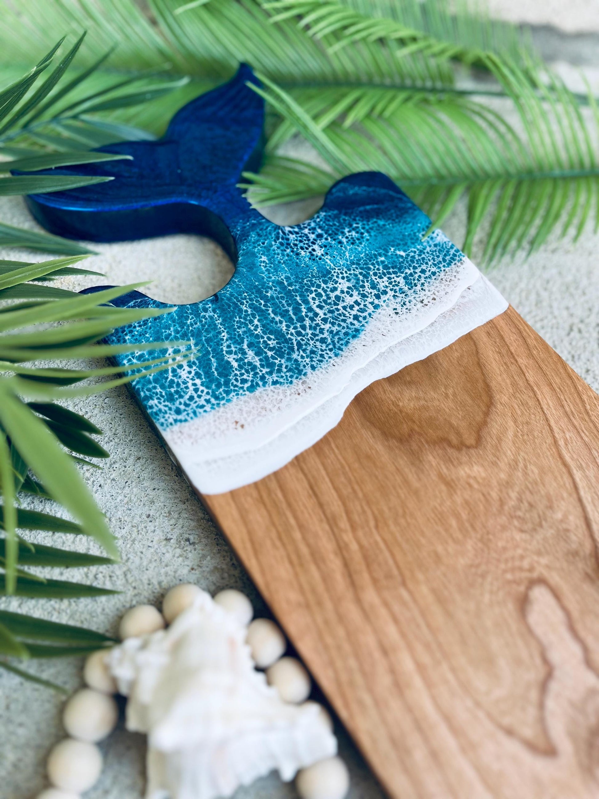 Cherry wooden charcuterie board with a mermaid tail fin shape at the top covered in blue and teal ocean resin waves.