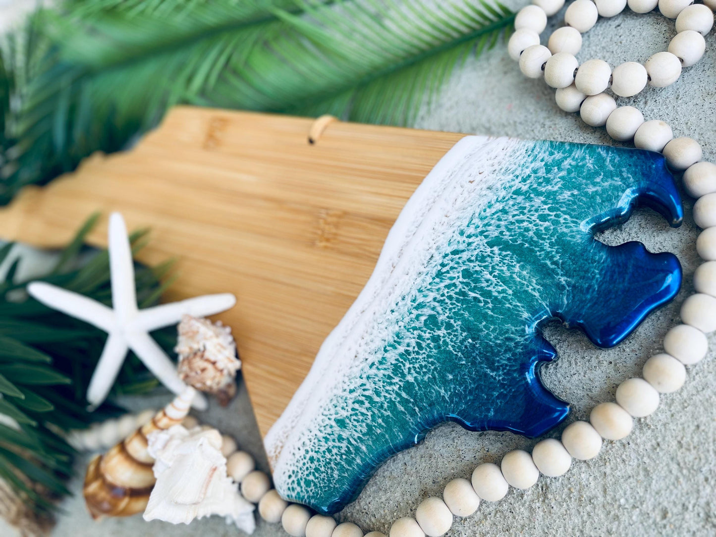 North Carolina shaped bamboo charcuterie board with blue and teal ocean resin waves along the coastline portion of the board