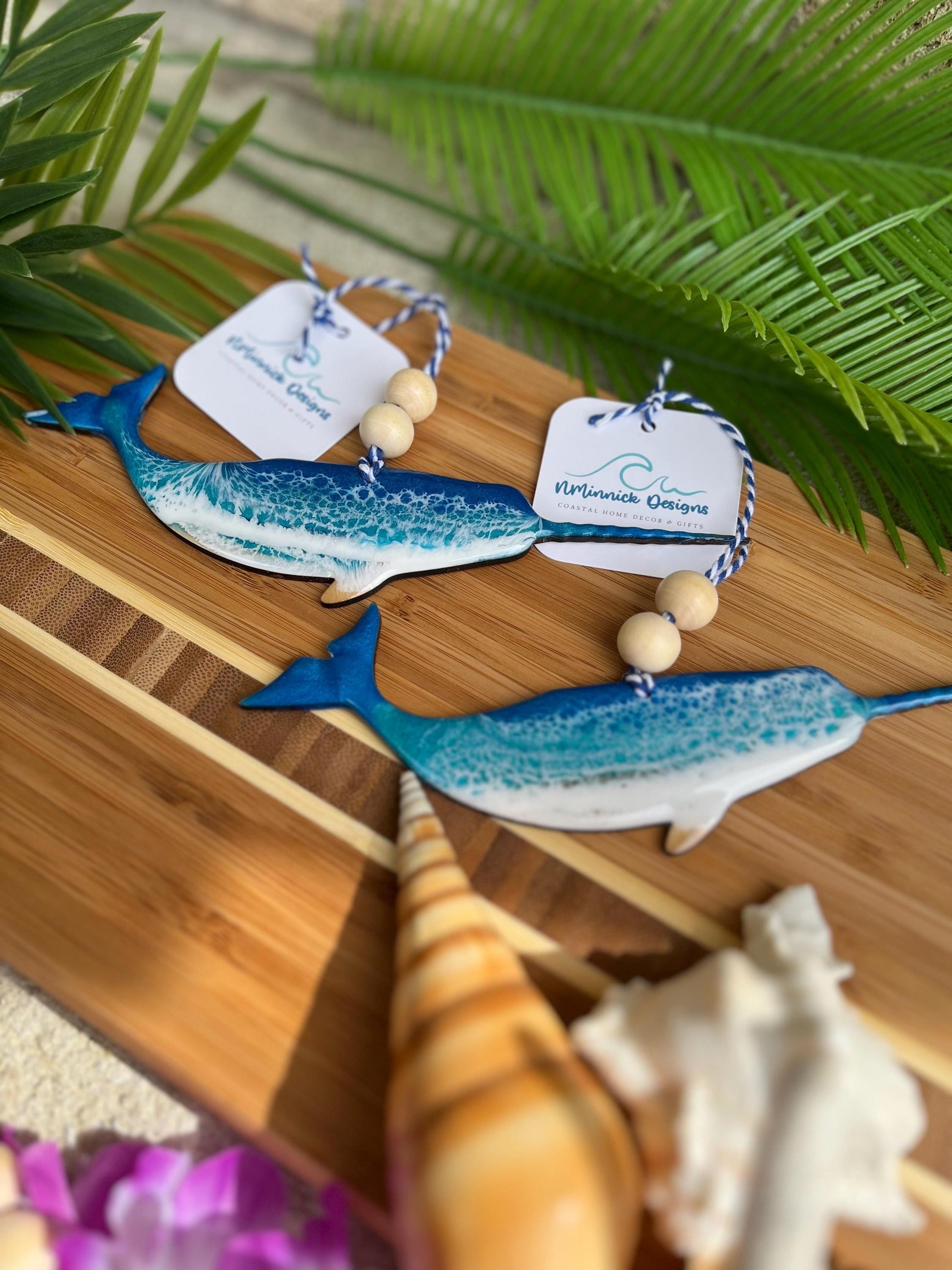 Narwhal shaped ocean ornaments laying on a bamboo board among palm trees
