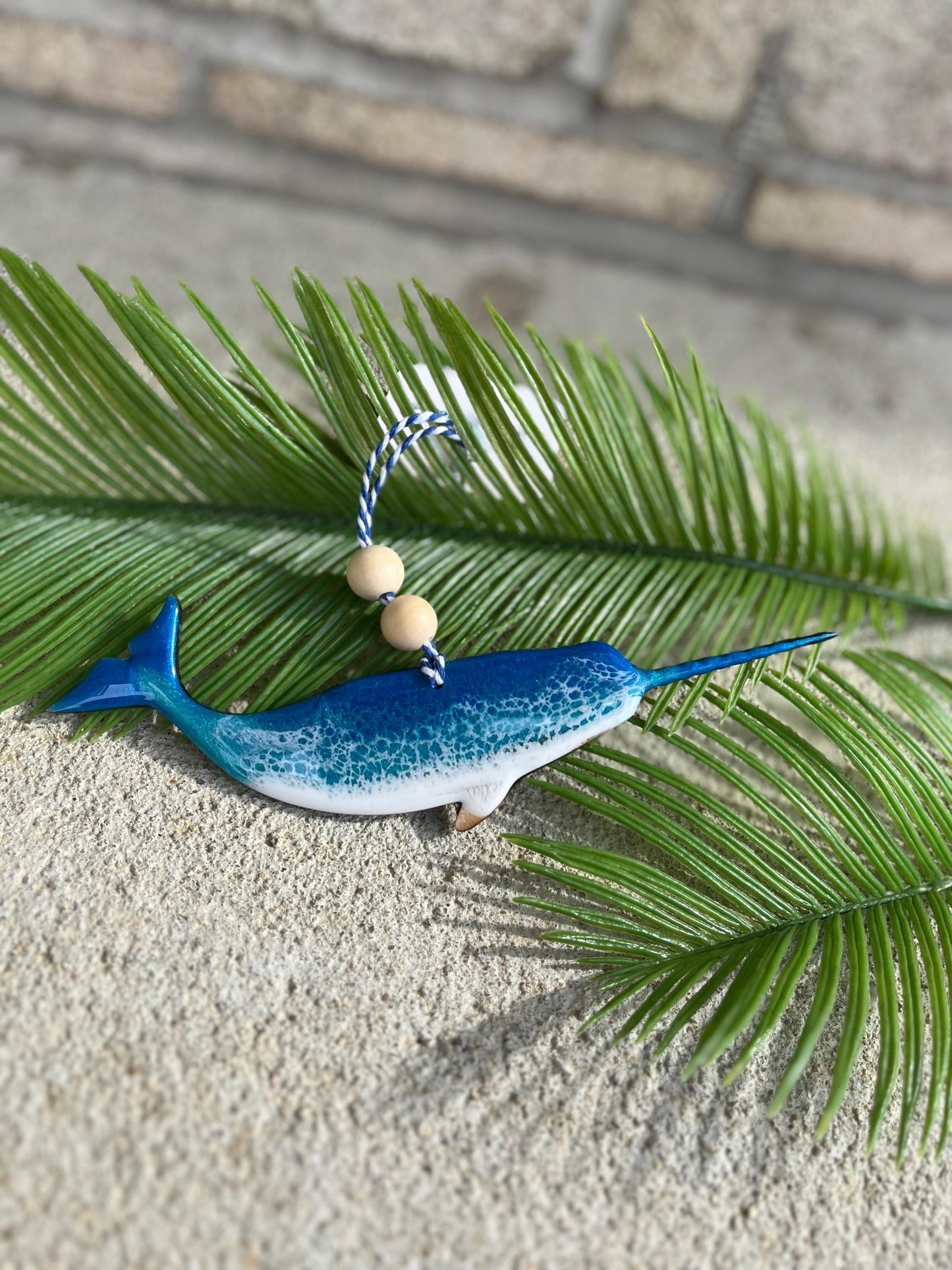 Narwhal shaped wood and resin ornament laying against palm leaves