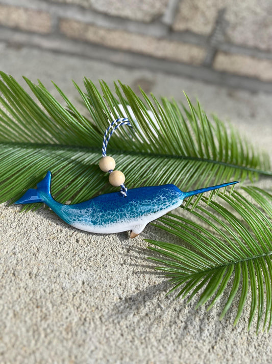 Narwhal shaped wood and resin ornament laying against palm leaves