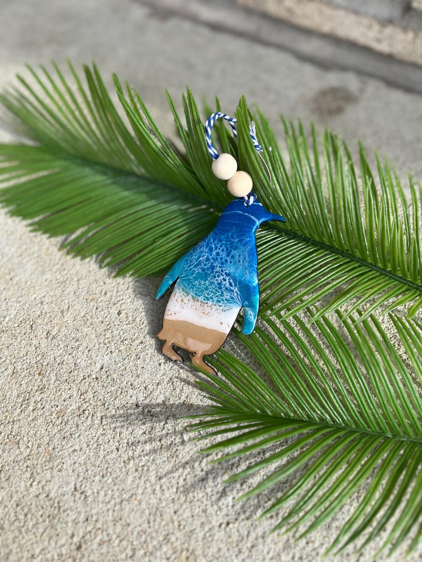 Penguin Ocean Resin Ornament laying against palm leaves